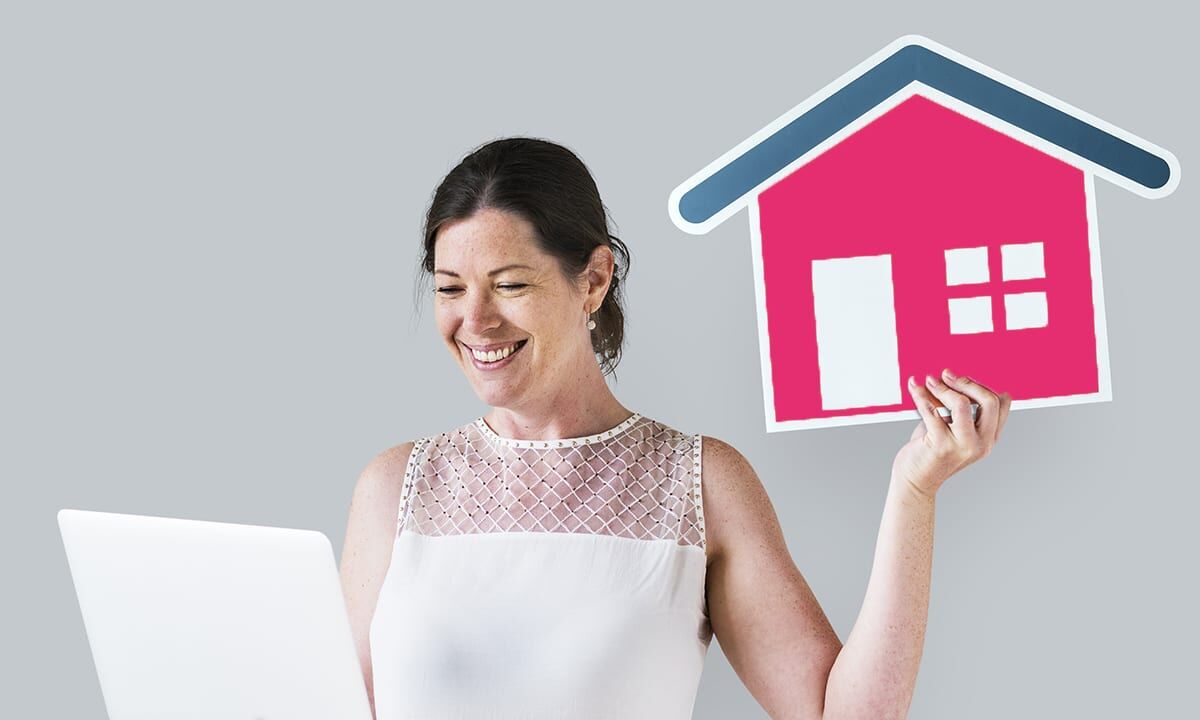 Woman holding a house icon and using a laptop